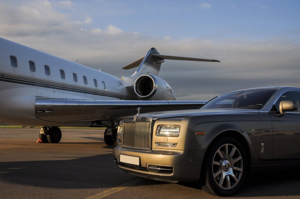 A luxury Rolls-Royce—part of a premium limo service Jacksonville, FL—awaits on an airport runway beside a sleek private jet under a partly cloudy sky.