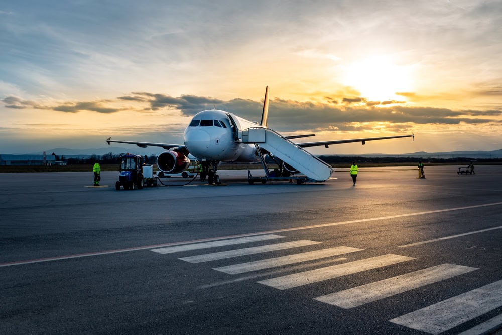 A commercial airplane is parked on the tarmac at sunset, with a mobile stairway attached and several people in high-visibility jackets working nearby. The scene is calm and quiet, perfect for travelers awaiting their Limo Service Jacksonville, FL.