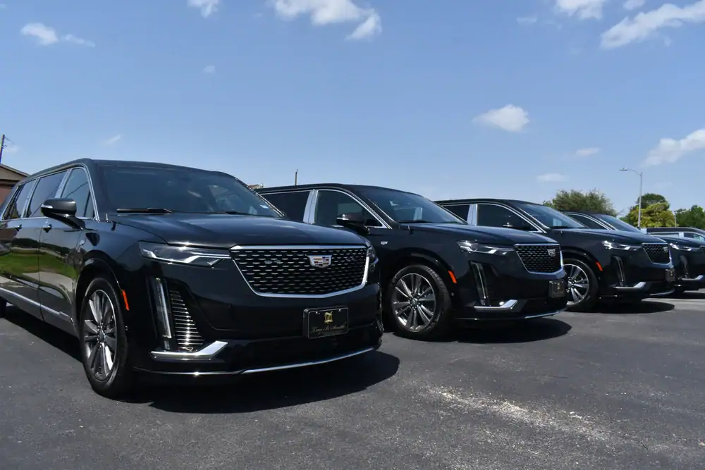 A row of shiny black Cadillac hearses and SUVs from a premier limo service New Jersey are parked on an asphalt lot under a blue sky with scattered clouds.