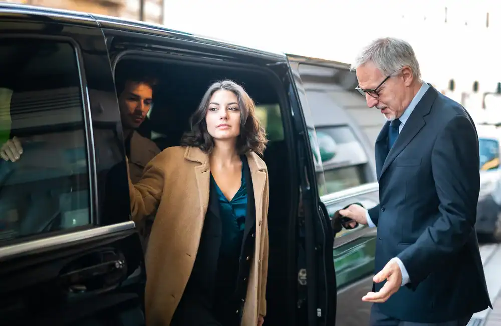 A woman steps out of a black car with the help of an older man in a suit, while another man sits inside. They appear to be arriving at a formal event, likely using a premium Limo Service New Jersey offers for such occasions.