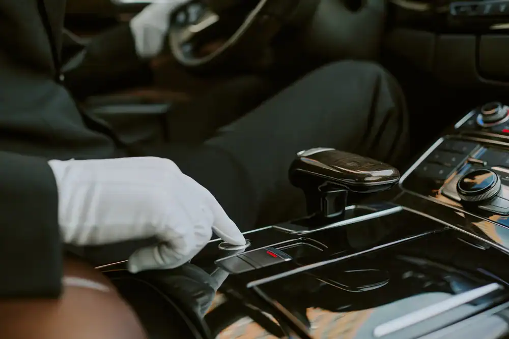 A person wearing white gloves presses a button on the glossy center console of a modern car&mdash;an attention to detail you expect from a premium Limo Service New Jersey, with the gear shift and dashboard controls visible.