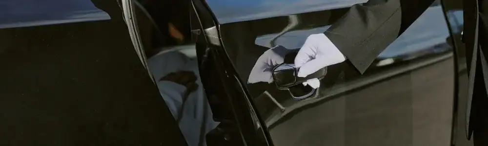 A person wearing white gloves and a suit opens the door of a black car, highlighting the luxury and professionalism of a Limo Service New Jersey.