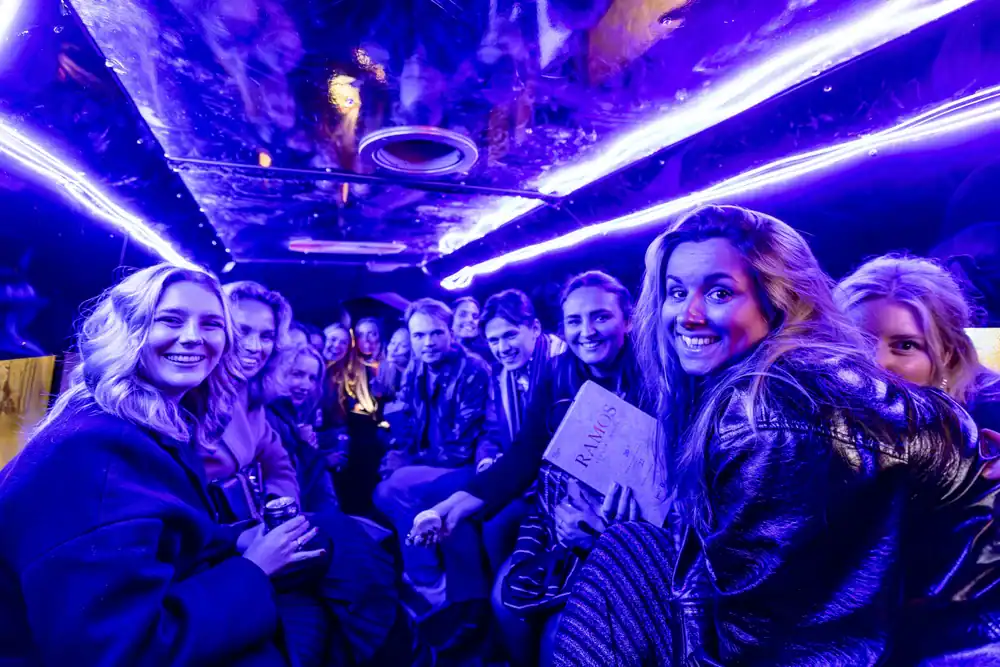 A group of people sit close together inside a party bus from a Limo Service New Jersey, illuminated by vibrant purple and blue neon lights, smiling and laughing as they enjoy the lively atmosphere.