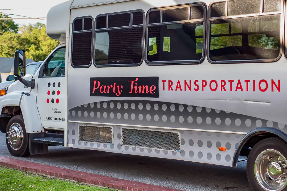 A white party bus with black windows and "Party Time TRANSPORTATION" written in red and black letters stands parked by a grassy area&mdash;perfect for anyone seeking premium Limo Service New Jersey for unforgettable group celebrations.